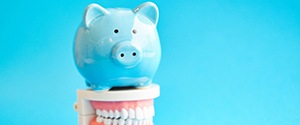blue piggy bank atop model teeth signifying cost of dental implants in Agawam
