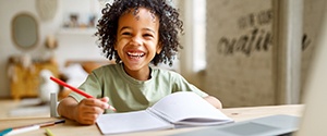 a smiling child sitting at a table and coloring