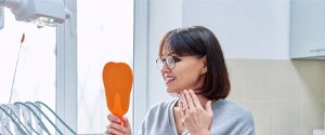 Woman in dental office, looking at her teeth in mirror