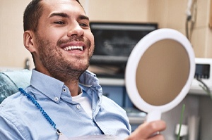 A young male wearing a blue button-down shirt and looking at his improved smile in the mirror