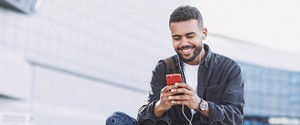 a smiling person sitting on a concrete structure and looking at their phone