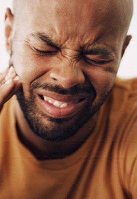 Man in yellow shirt squinting and touching hand to jaw in pain