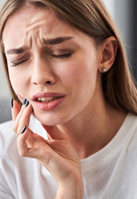 Woman in white shirt touching jaw in pain with eyes closed