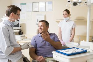 smiling man in dental chair talks to dentist