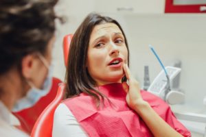 Woman in dentist chair holding the side of her mouth in pain