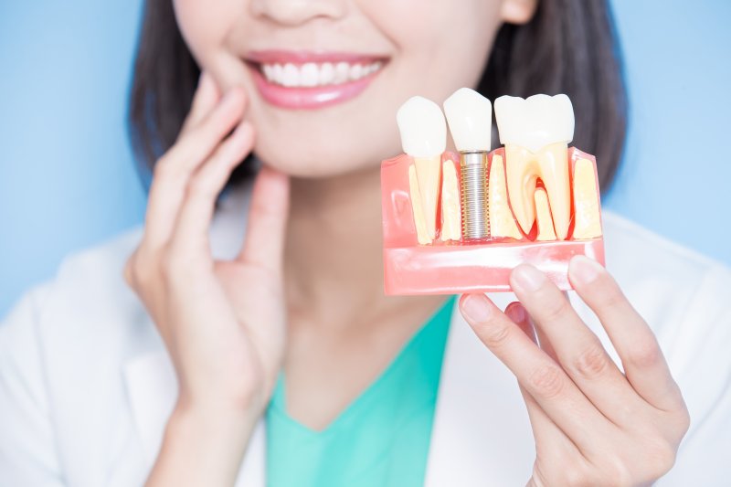 dentist holding dental implant model and smiling