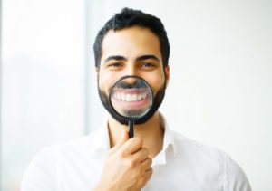 man showing off the results of his teeth whitening after braces with a magnifying glass
