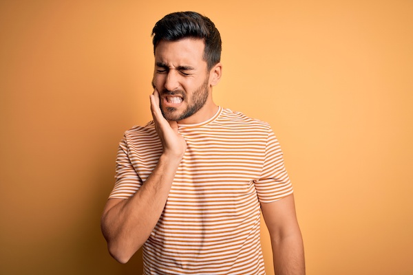 dark haired man with a toothache orange background