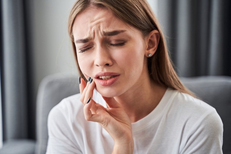 Young woman holding her right cheek with her hand and grimacing