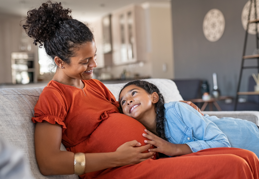 Pregnant mom relaxing on couch with young daughter